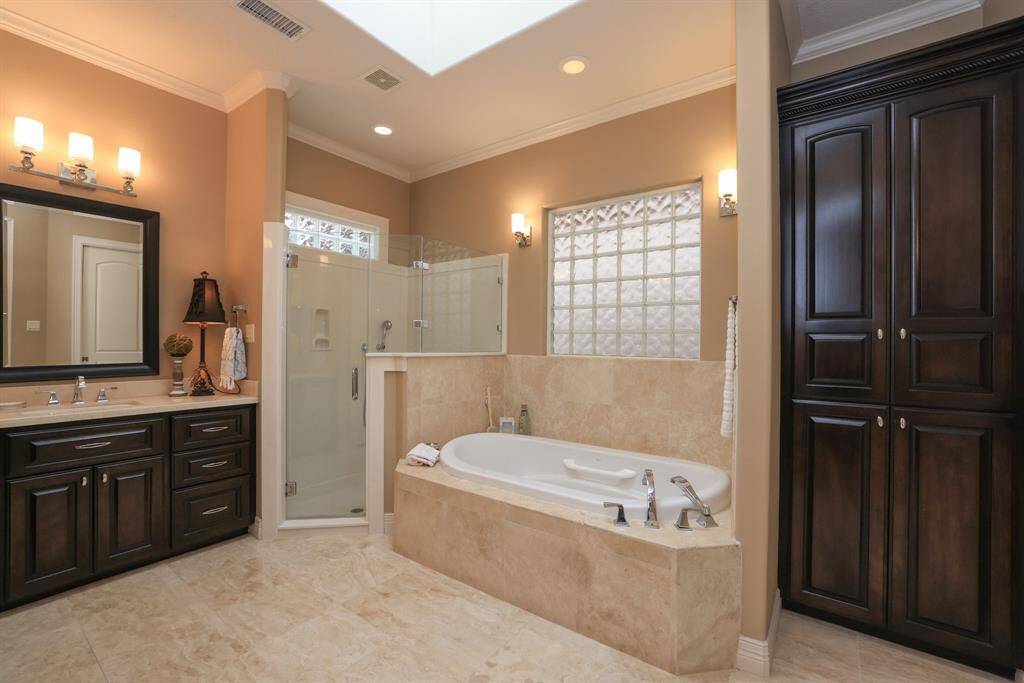 The spacious bathroom features a luxurious Ultra Bain tub, a separate glass-enclosed shower, and rich dark wood cabinetry.  To the right is a large built in custom cabinet.