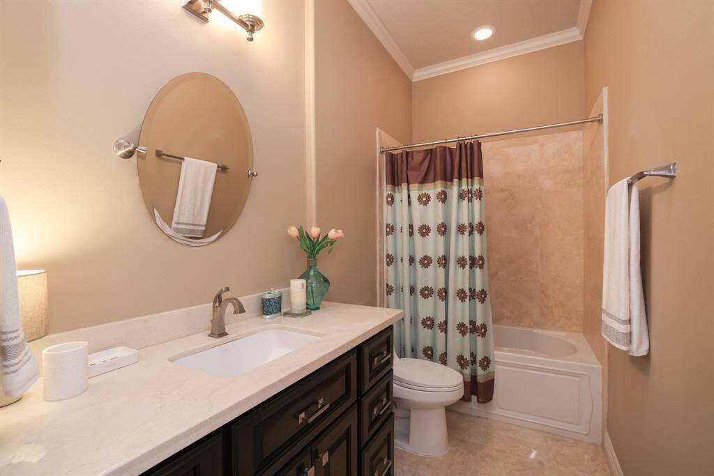 Experience modern elegance in this bathroom with a dark wood vanity, marble countertop, and distinctive round mirror. Enjoy the convenience of a bathtub/shower with tile surround, sleek tile flooring, and recessed lighting.