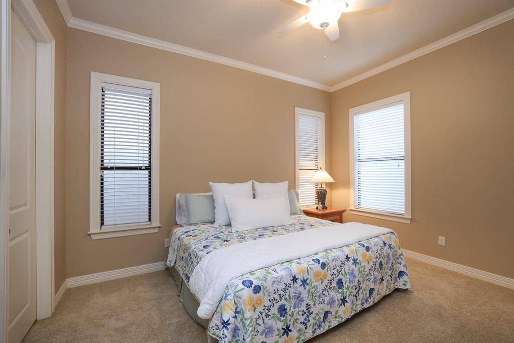 Bedroom #3 offers soft beige walls, plush carpeting, and abundant natural light from three windows, complemented by a lighted ceiling fan.