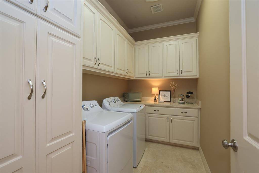 This photo shows a well-organized laundry room with ample storage, including a broom closet! It features built-in cabinets,  and a countertop to fold clothing. The space is efficiently designed with tile flooring.
