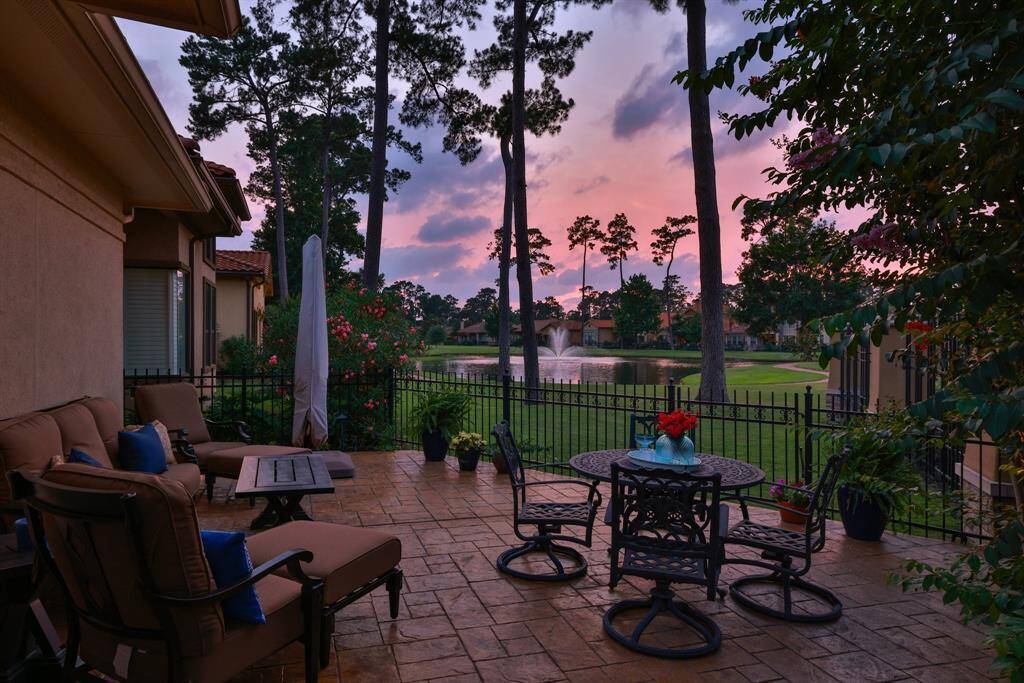 This is a view of the beautifully landscaped garden with neatly trimmed hedges and vibrant flowers. A pathway leads to a statue and a fountain in a pond, surrounded by lush greenery and elegant homes, creating a serene and picturesque setting.