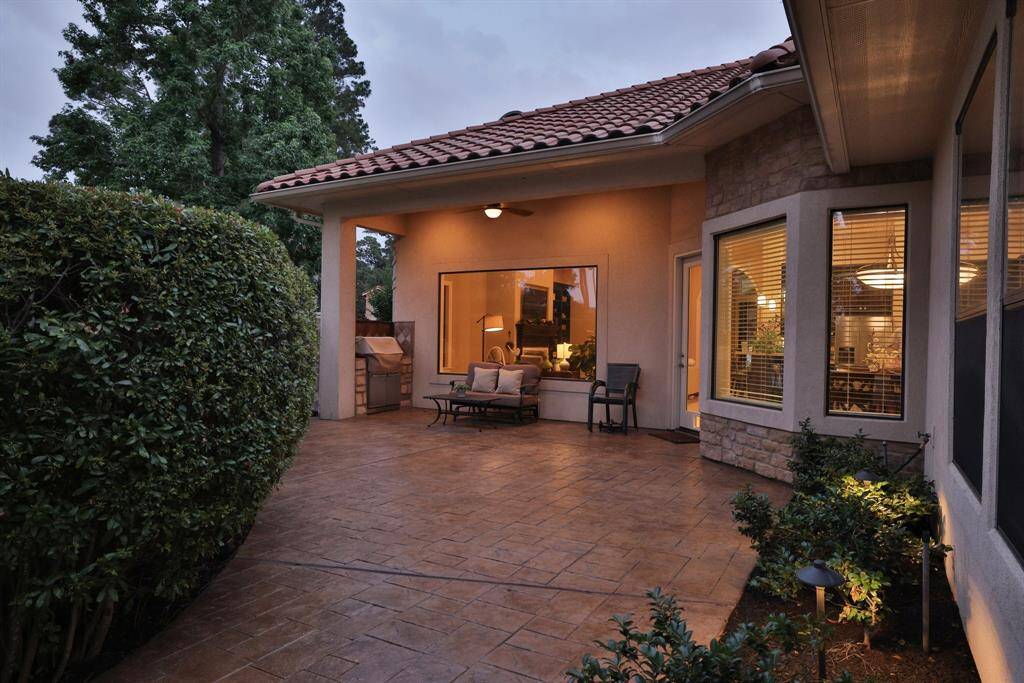 Another view of the charming backyard patio with a tiled roof, surrounded by a black iron fence. It features comfortable outdoor seating and a row of hedges for privacy!