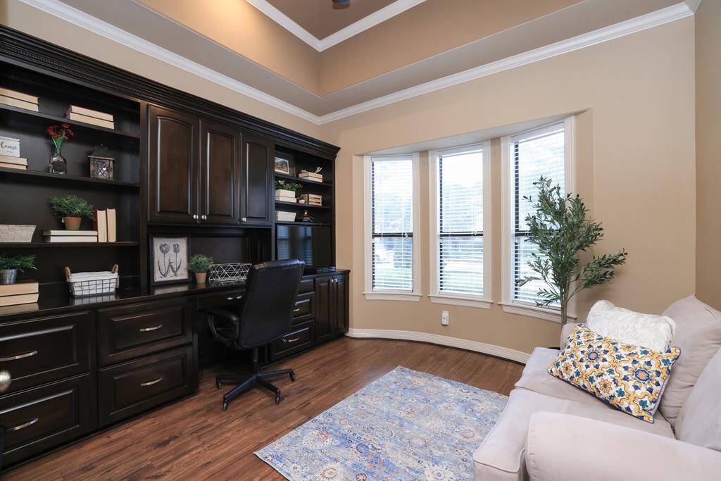 This home office features a fabulous dark wood built-in shelving and cabinets, andd a large bay window for natural light. The space is complemented by warm wall tones and wood flooring, creating a comfortable and functional work environment.