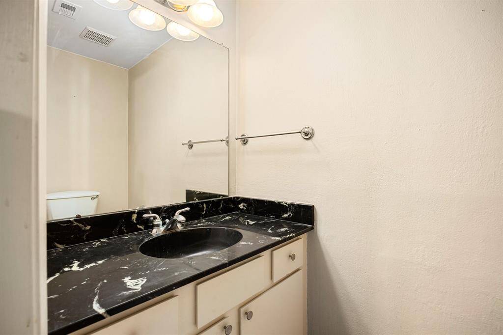 A sleek and functional secondary bathroom highlighted by a striking black marble vanity, neutral-toned walls, and bright overhead lighting—offering both style and convenience.