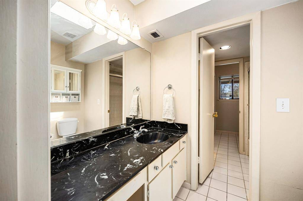 This primary bathroom showcases a bold black marble vanity, bright overhead lighting, and a well-designed layout—creating a serene space to begin and end each day.