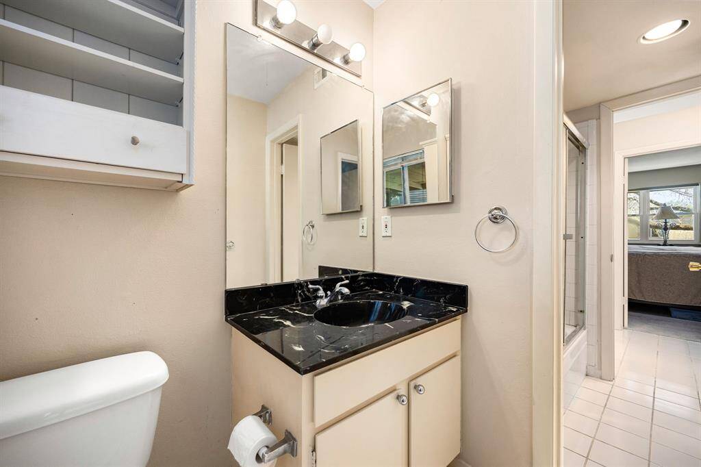 A well-appointed secondary bathroom featuring a striking black marble vanity, bright lighting, and built-in shelving—creating a stylish, convenient space to start and end your day.