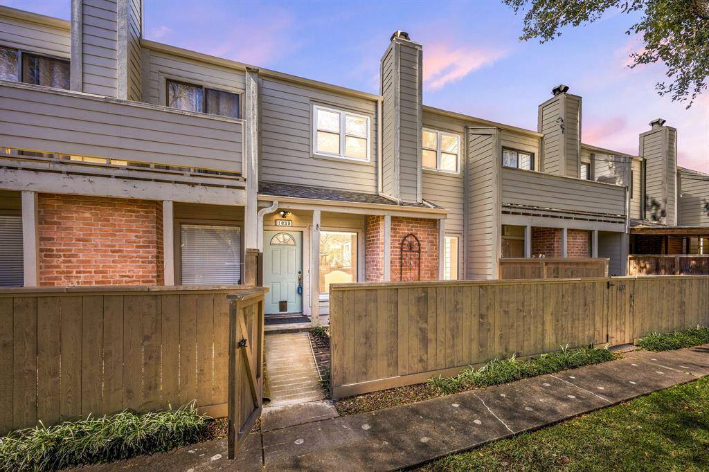 This charming two-story townhome boasts partial brick siding, a fenced courtyard, and is nestled under mature shade trees, creating inviting curb appeal in a serene community setting.