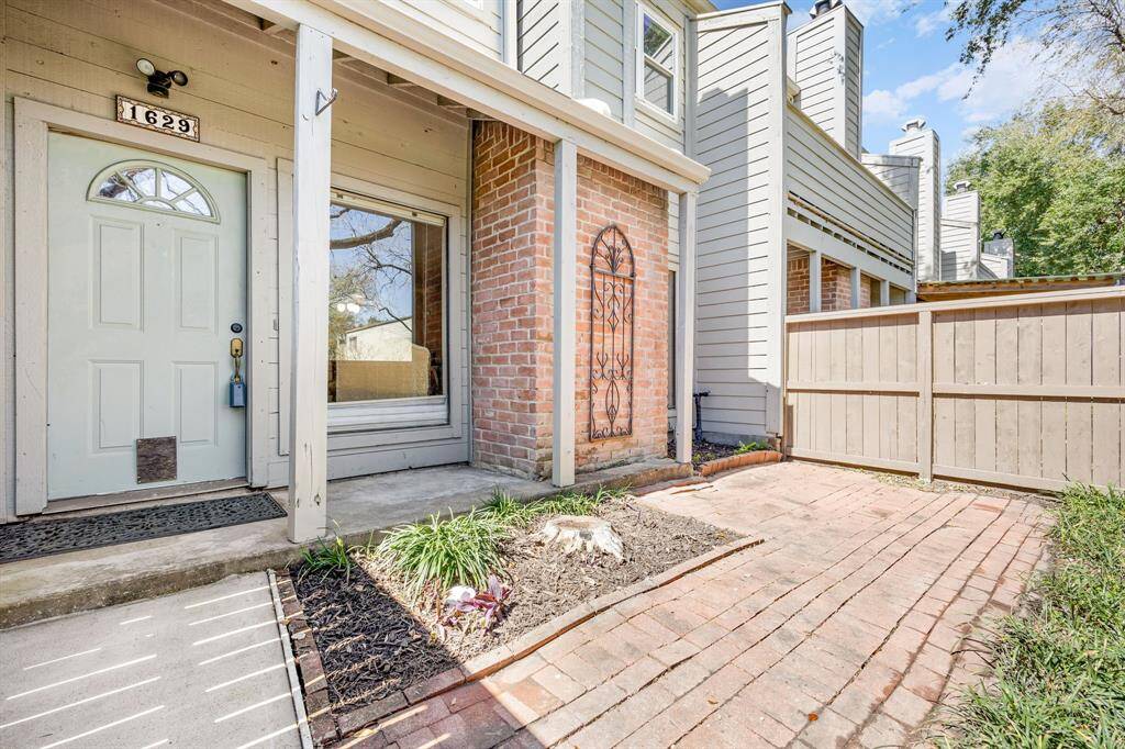 A welcoming front entrance with partial brick detail and a stylish door—set behind a fenced courtyard for added privacy and curb appeal.