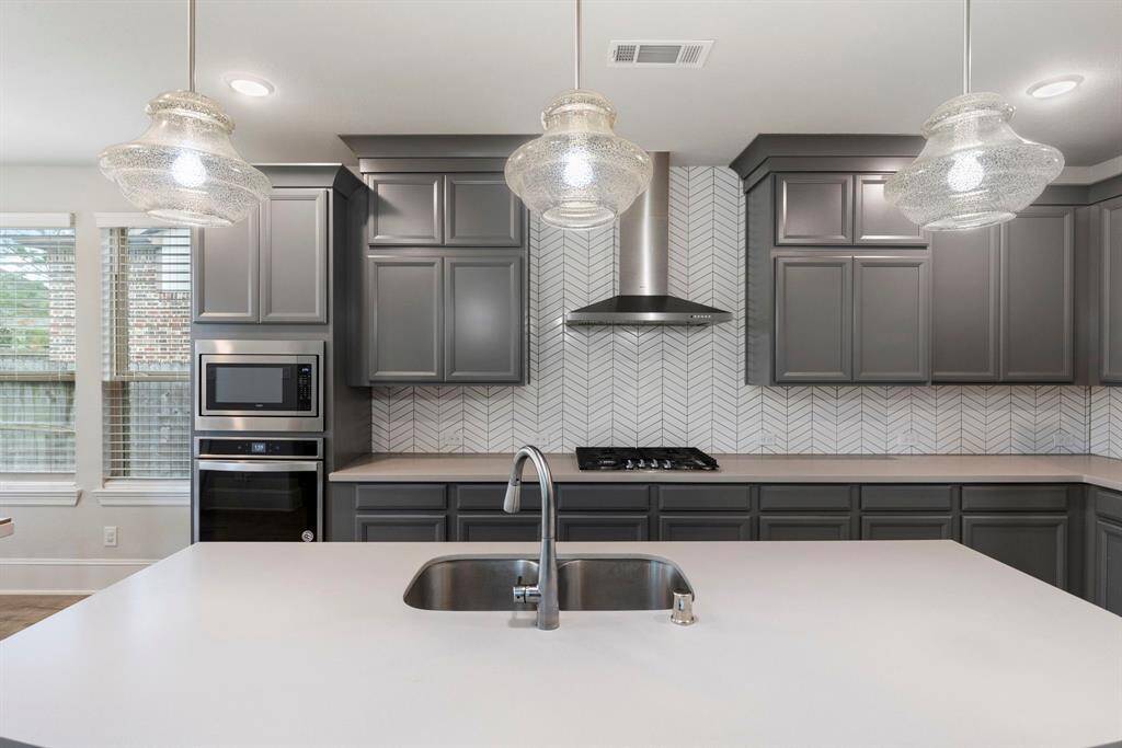 A gas cooktop and vent are the focal points in the stunning kitchen, along with the exquisite quartz counters and gorgeous chevron pattern tile backsplash.