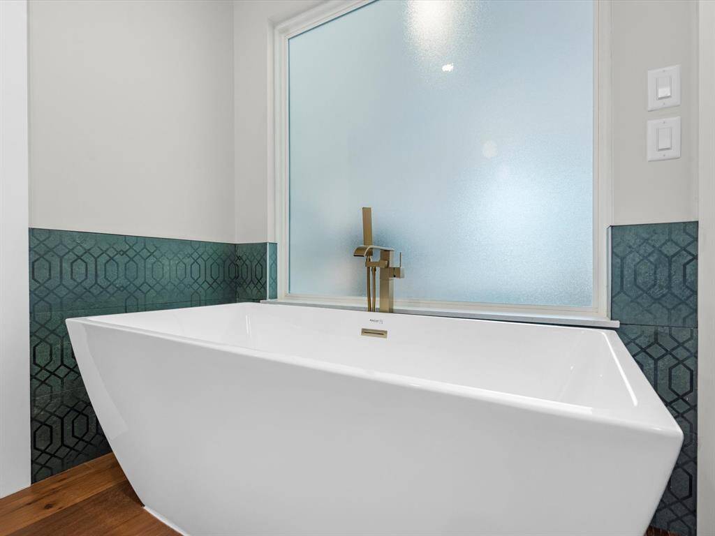 The primary bathroom showcases a large soaking tub complemented by designer gold plumbing fixtures and elegant wall tiles, creating a spa-like retreat.