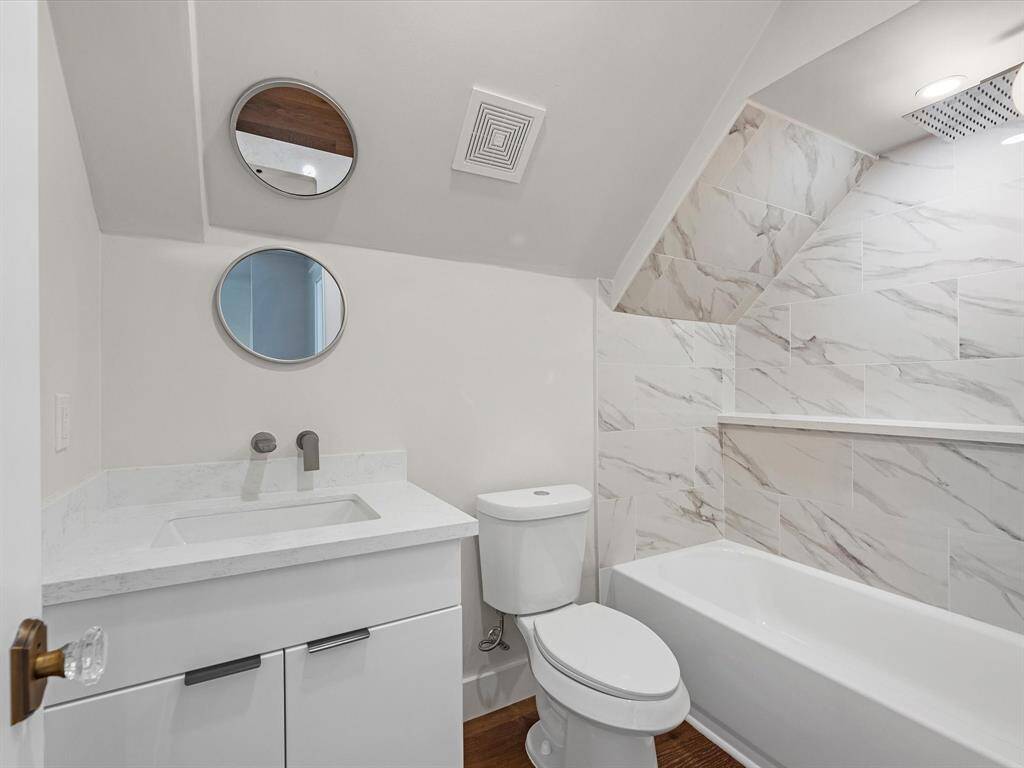 The upstairs bathroom features a sleek vanity with quartz countertop, modern fixtures, marble-inspired wall tiles, a built-in shower shelf, and a relaxing tub, combining elegance and practicality.