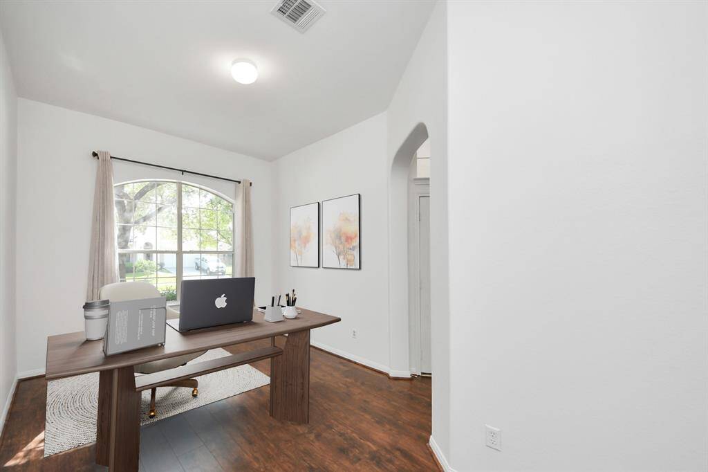 Versatile front room perfect for a home office, featuring a large arched window and wood-look flooring. (virtually staged)