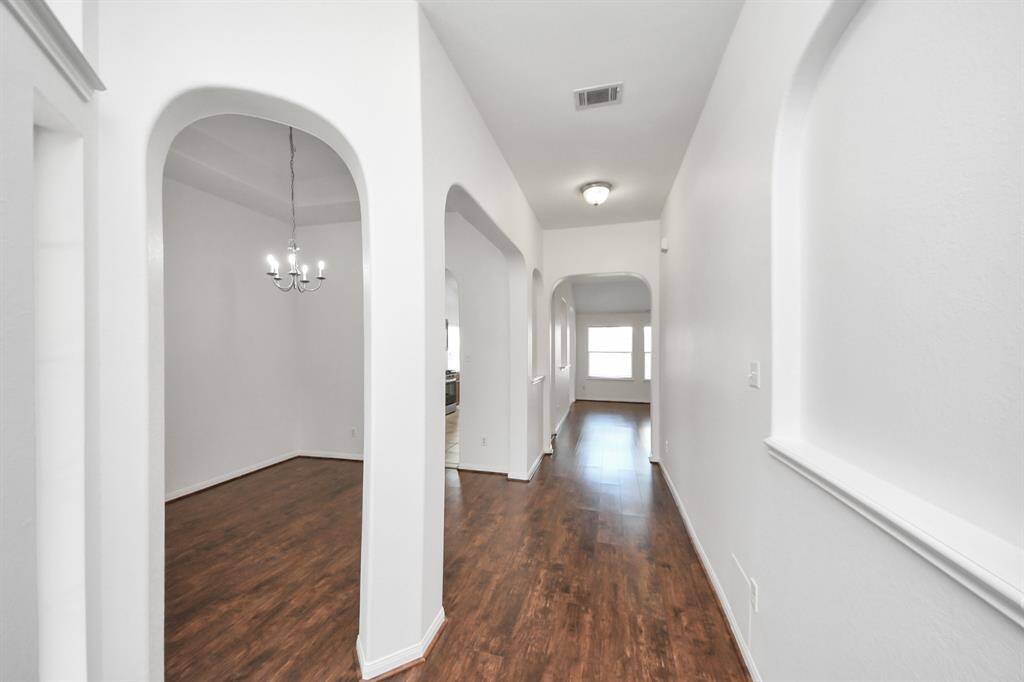 Inviting hallway with rich flooring, architectural archways, and art niches leading to the main living area.