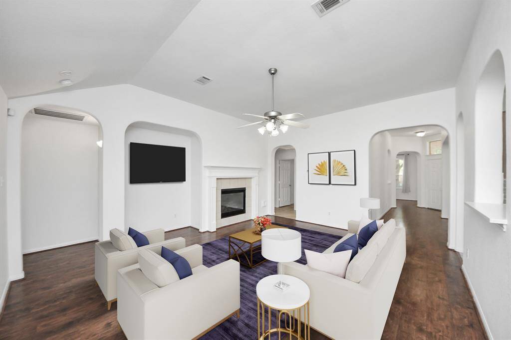Spacious family room with cozy fireplace, high ceilings, and multiple arched entryways—perfect for entertaining. (virtually staged)
