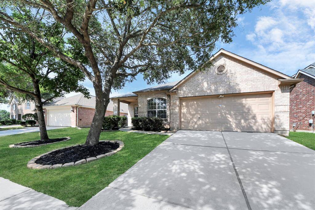 Spacious driveway and two-car garage framed by mature trees and manicured greenery.
