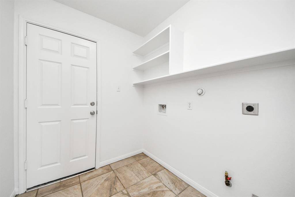 Functional laundry room with upper shelving, tile floors, and garage access.