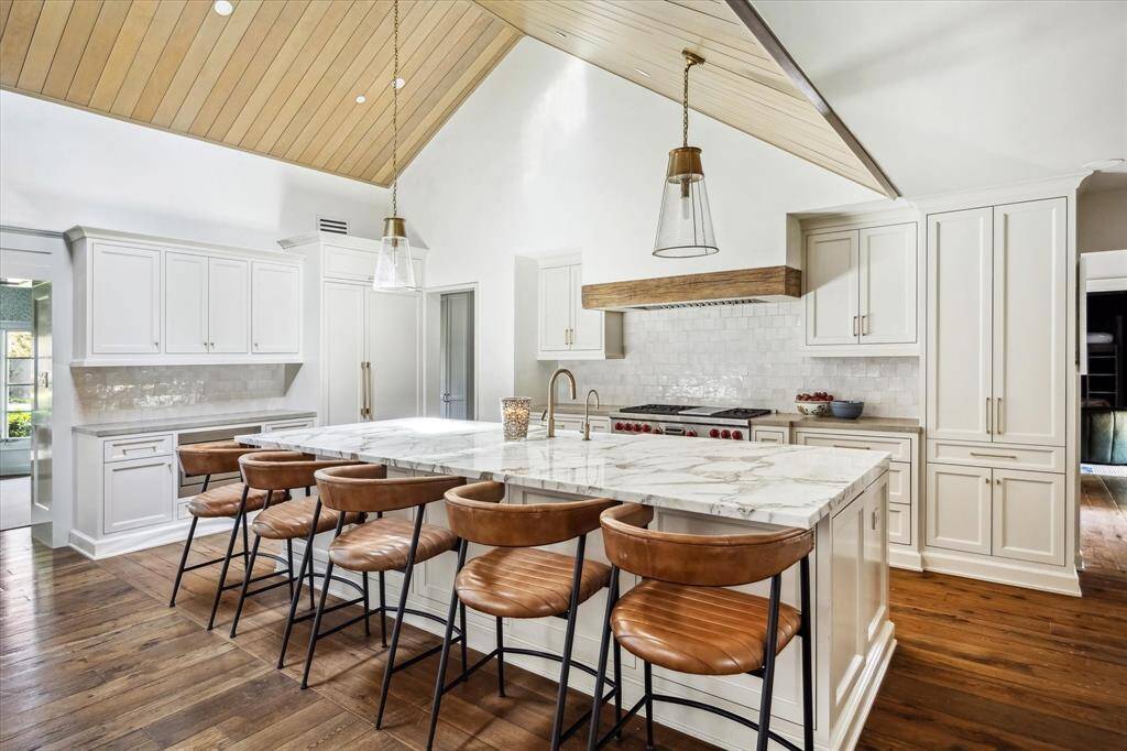 The kitchen features a large working island with an undermount farm sink, stainless steel Wolf and SubZero appliances, vaulted wood-paneled ceilings, and ample storage space.