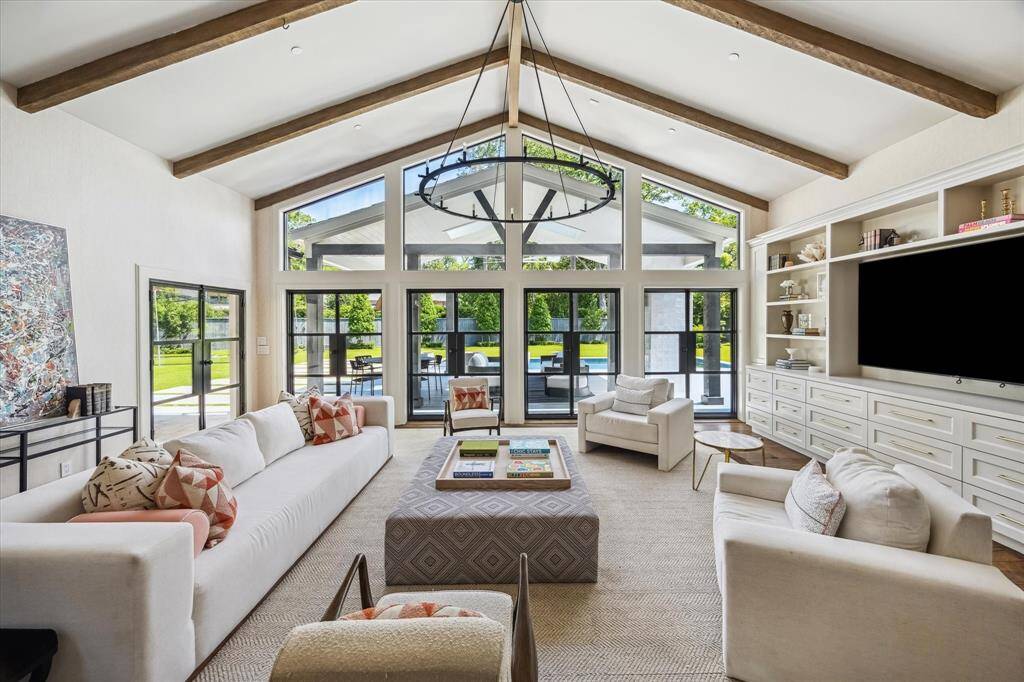The family room offers views of the backyard through steel-framed doors, vaulted ceilings with wood beams, and numerous built-ins.