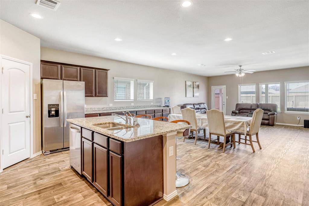 The open floor plan effortlessly connects the kitchen, dining, and living areas, unified by rich vinyl plank flooring and recessed lighting that lends a polished, contemporary vibe.