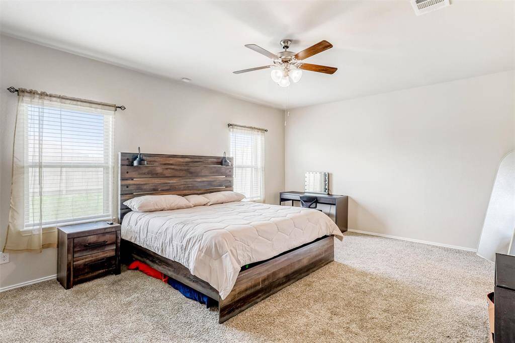 Spacious and peaceful, the primary suite features plush carpeting, a ceiling fan, and large windows that filter in soft morning light—offering a quiet escape at the end of the day.