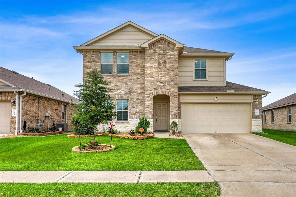 A blend of brick and stone creates a timeless facade, while manicured plant beds, a young tree, and a well-kept lawn frame the home with a welcoming touch.