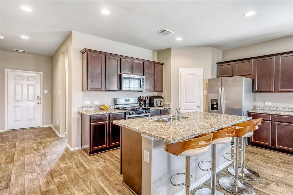 Granite countertops, dark wood cabinetry, and stainless steel appliances define this culinary space. The oversized island, complete with seating and a deep sink, invites conversation and casual meals, while keeping the cook at the center of the action.