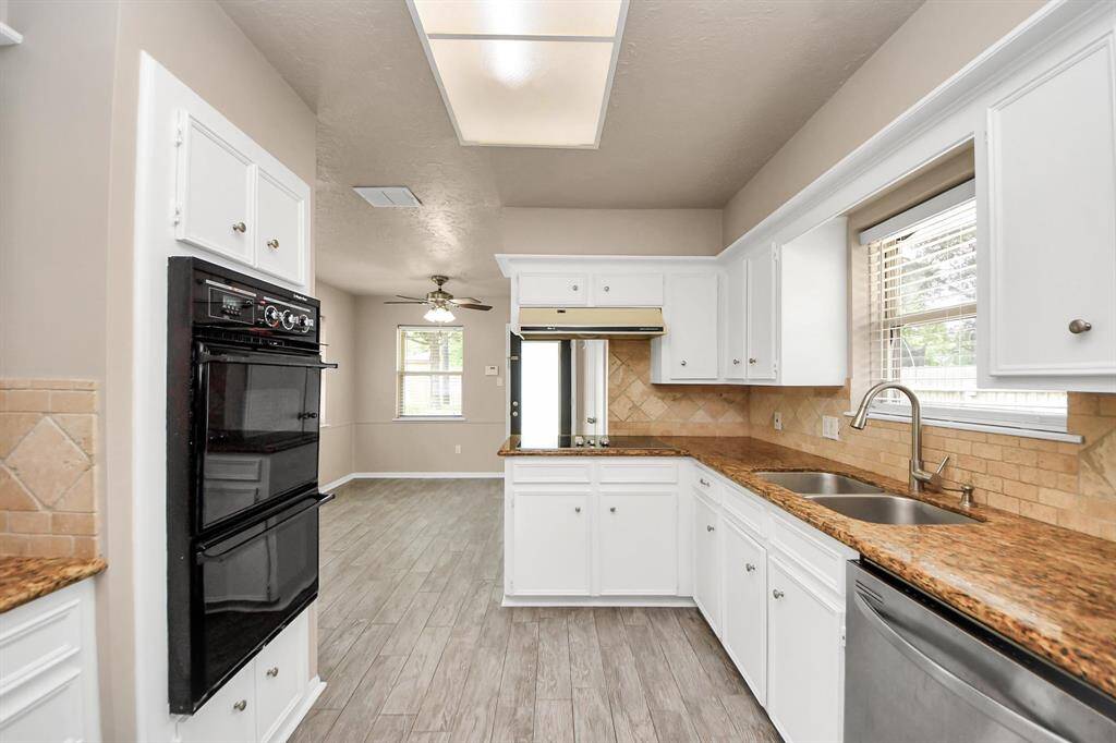 The kitchen boasts built-in double ovens, granite countertops, a travertine backsplash, and a sleek glass cooktop—combining style and functionality for the modern home chef.