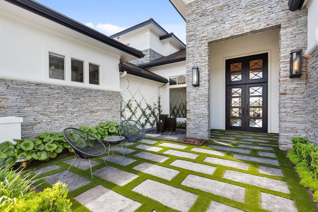 The front courtyard is a private, enclosed oasis, featuring meticulously laid stone flooring contrasted by lush artificial turf, creating a welcoming and low-maintenance outdoor space.