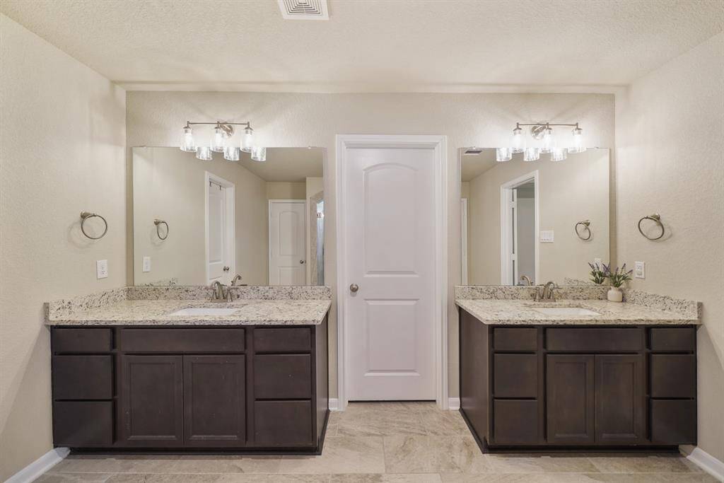 Dual sinks with granite countertops and backsplash,a large mirror, and elegant lighting.