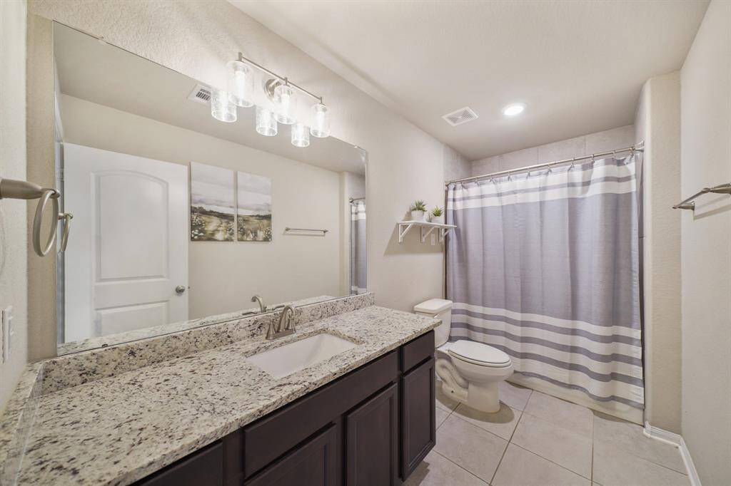 Secondary bathroom with tile floors, granite countertops and backsplash, wooden cabinetry, and a shower/tub combo.