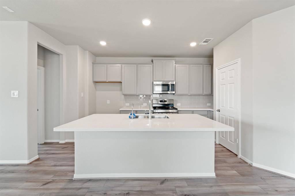 This light and bright kitchen features a large quartz island, white cabinets, a large sink overlooking your family room, recessed lighting, and beautiful backsplash.