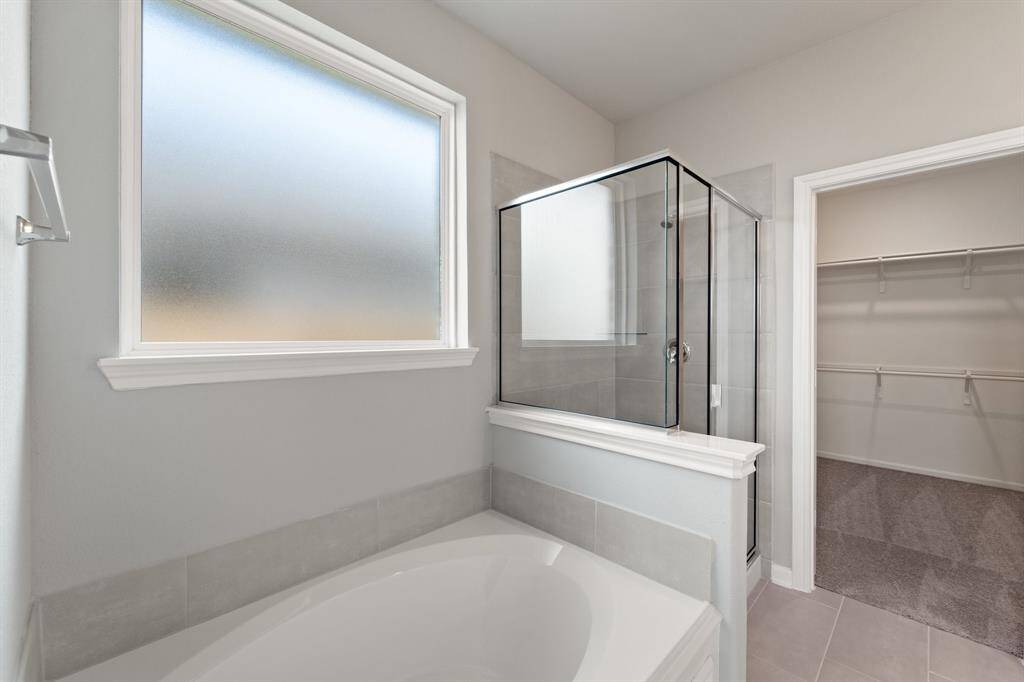 This additional view of your primary bathroom features tile flooring, fresh paint, walk-in shower, a separate garden tub, and a large walk-in closet.