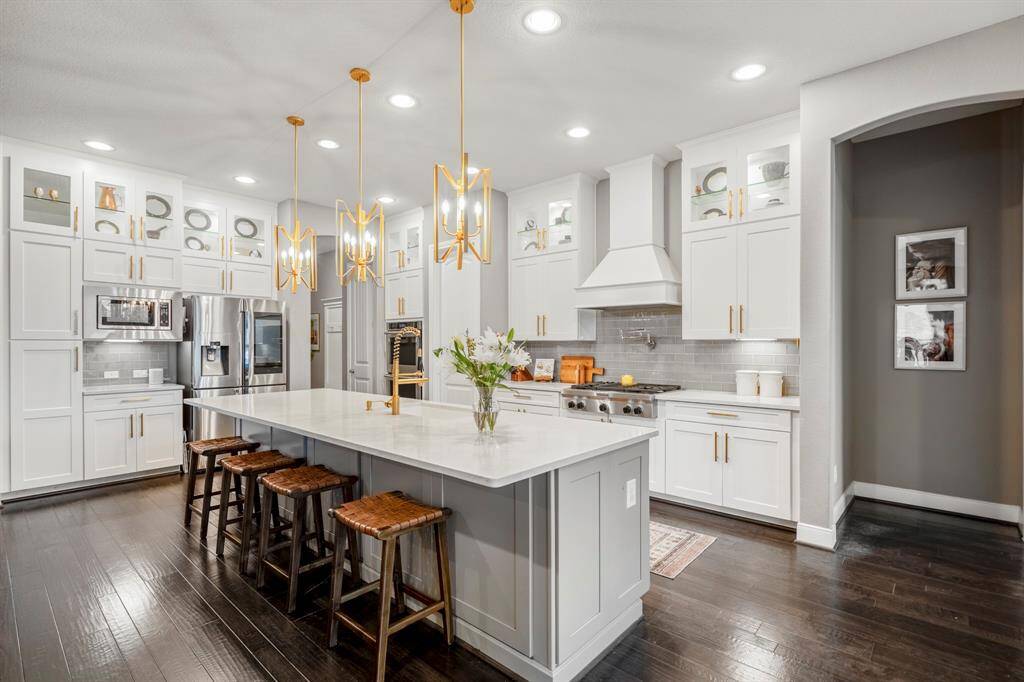 The kitchen boasts a deco wood paneled island with a sleek gold faucet and large single basin sink. Upgraded with extended glass paneled cabinets, built-in stainless steel appliances, quartz countertops, double ovens, this kitchen is ideal for cooking for the whole family or hosting holidays!