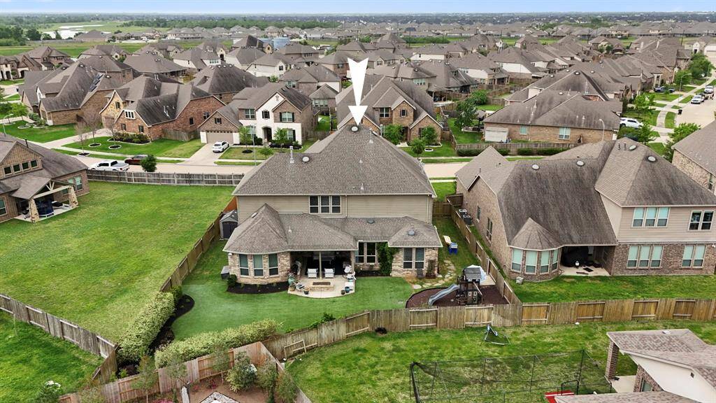 This aerial view showcases a spacious backyard that includes a playground, putting green, oversized outdoor covered patio, outdoor kitchen, fire pit, and turf!