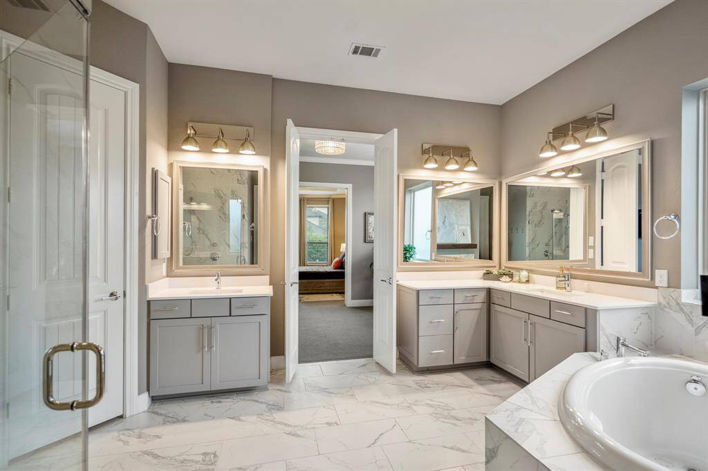 Experience luxury in this expansive primary bathroom, complete with separate vanities, dual sinks, framed mirrors, and sleek quartz countertops.