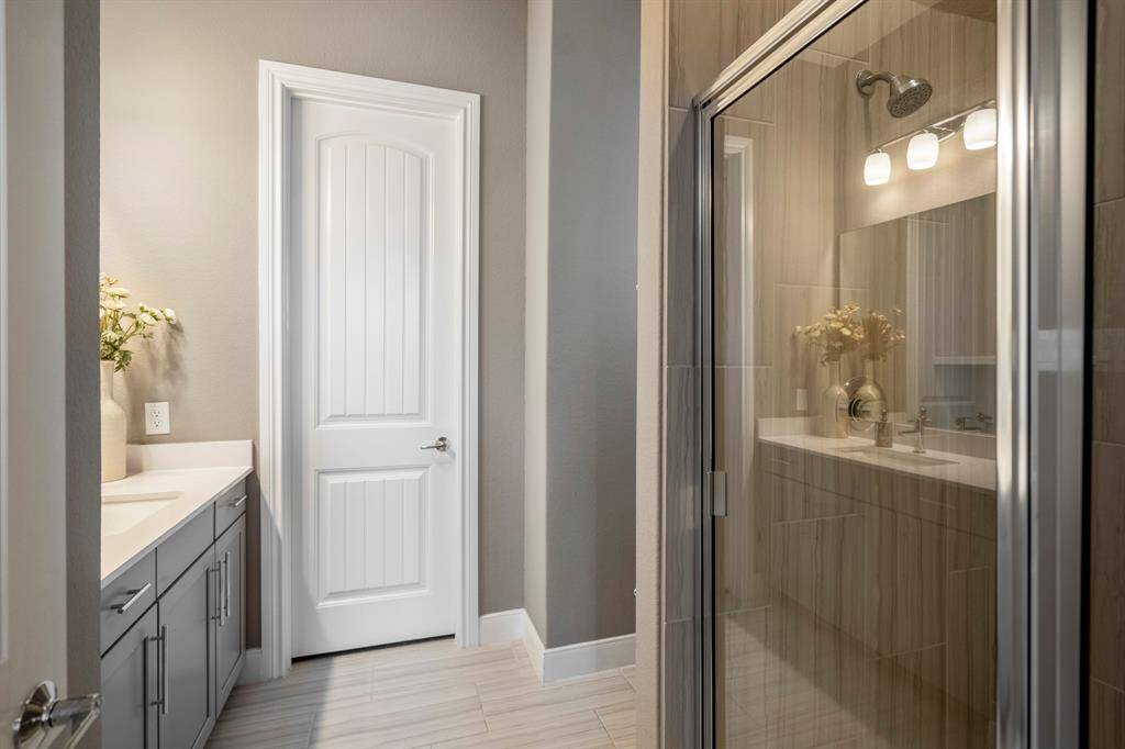 The downstairs full bathroom with wood stained cabinets, quartz countertops, a spacious walk-in shower, and large vanity, is located just off the downstairs secondary bedroom, making it a perfect place for guests to unwind.