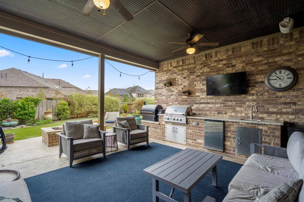 The expansive covered patio is designed for year-round enjoyment, featuring dual ceiling fans, built-in speakers, and a fully equipped outdoor kitchen. The kitchen boasts a built-in gas grill, additional sink, granite countertops, and a smoker.