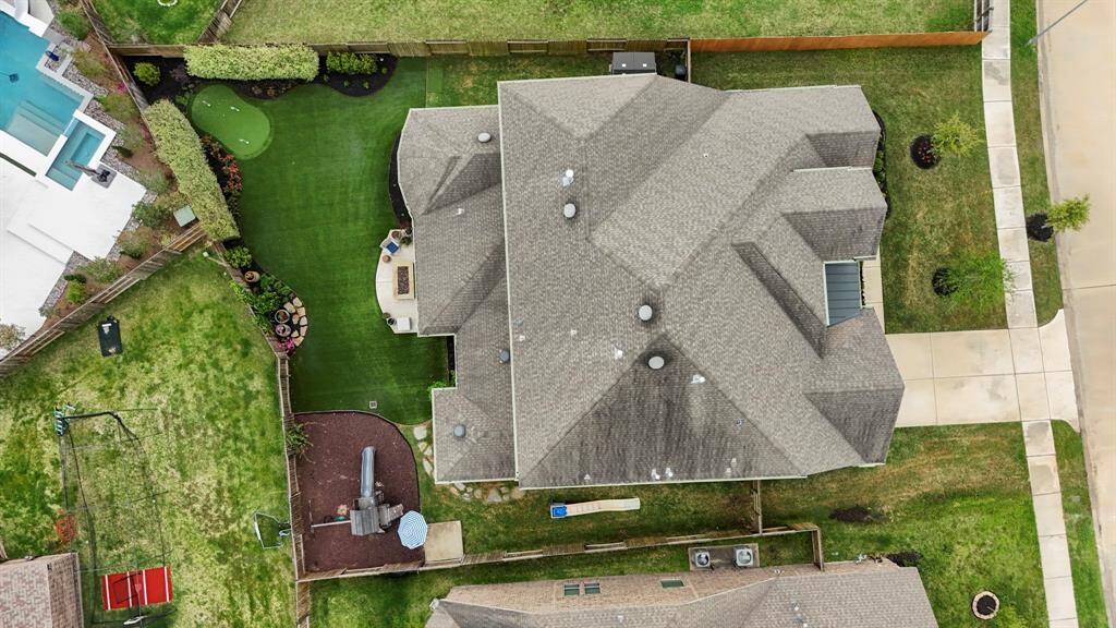 This sweeping aerial shot highlights the beautifully landscaped backyard, featuring custom landscaping, lush artificial turf, a dedicated play area, and expertly installed French drains.