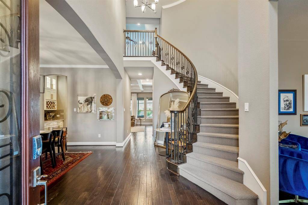 Walking in, you're welcomed into an elegant entryway with stunning wood floors, spiral staircase, and chandelier. The high ceilings, crown molding, open design, and natural light create a warm, welcoming atmosphere, setting the perfect tone for the rest of the home.