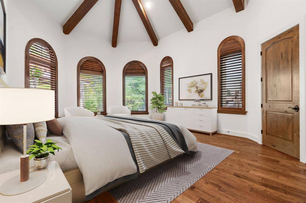(VS) The primary suite impresses with warm wood flooring, a beamed and octagon-shaped ceiling, and elegant arched windows that frame serene views of the lush backyard.