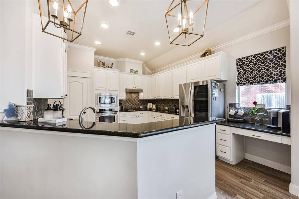 A kitchen featuring elegant granite countertops, a stylish tile backsplash, recessed lighting, and tall cabinets adorned with crown molding for a polished finish.