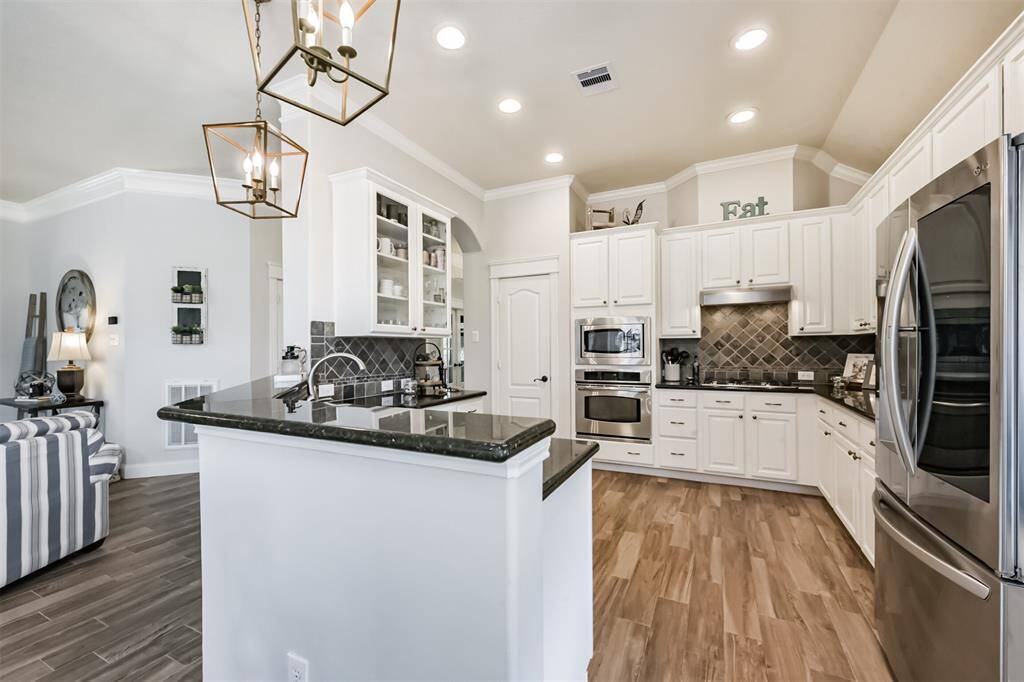Stainless steel appliances, a direct-vent cooktop, a walk-in pantry, and a set of cabinets with elegant glass panels combine to create a functional yet sophisticated kitchen space.