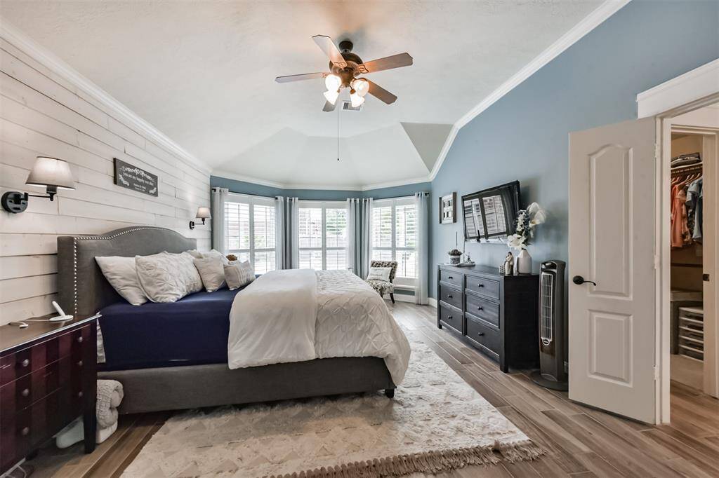 The primary bedroom boasts elegant bay windows, a striking gambrel ceiling, a ceiling fan with a light fixture, and a charming shiplap accent wall.