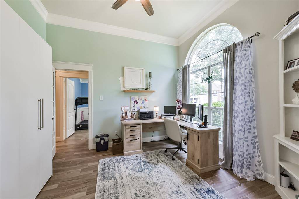 A sophisticated office or study featuring elegant triple crown molding and a large, graceful arched window.