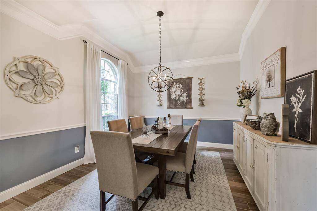 Elegant formal dining room featuring triple crown molding and chair rail detailing, complemented by a stylish designer light fixture.