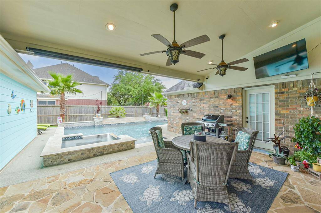 Covered back patio featuring recessed lighting and elegant flagstone flooring, offering a serene view of the hot tub and swimming pool.
