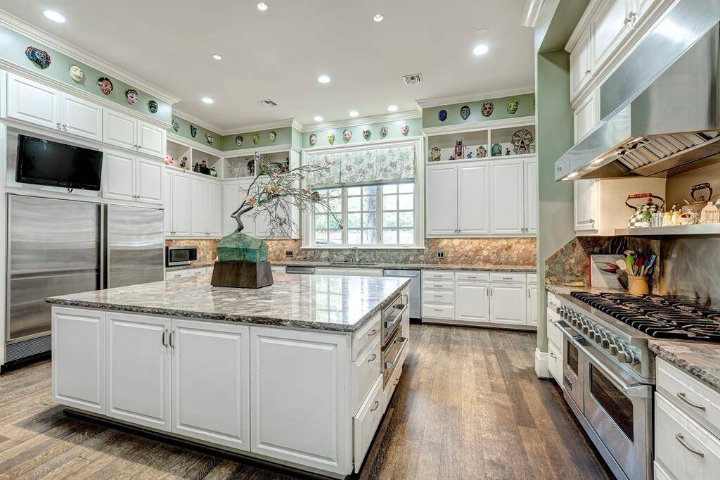 One of the most impressive features of this kitchen is the wide variety of professional appliances. It includes an industrial range with a hood vent, elegant hardwood flooring, and a granite countertop. The overall design provides ample usable space, making it ideal for entertaining.