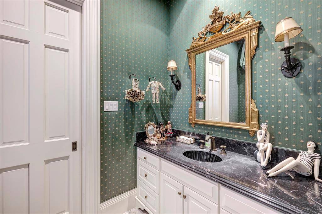 The first-floor powder room is furnished with an elegant mirror, marble countertops, marble flooring, and sconces, enhancing the aesthetic and functional qualities of the space..