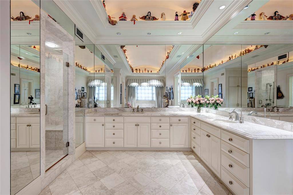 The primary bath has a domed ceiling with cove lighting, marble vanities with two sinks, pretty marble flooring, and a walk-in shower with a seat.