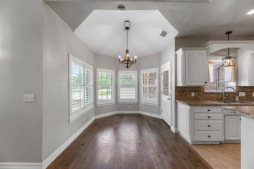 Just off the kitchen, the charming breakfast area is surrounded by windows with plantation shutters, filling the space with natural light. A statement light fixture and warm wood flooring add the perfect finishing touches.